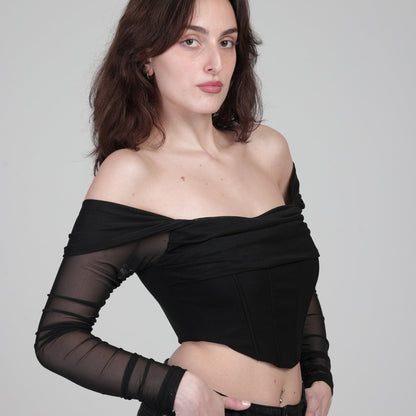 model in black corset top with sleeves shows side of product, in front of white background.
