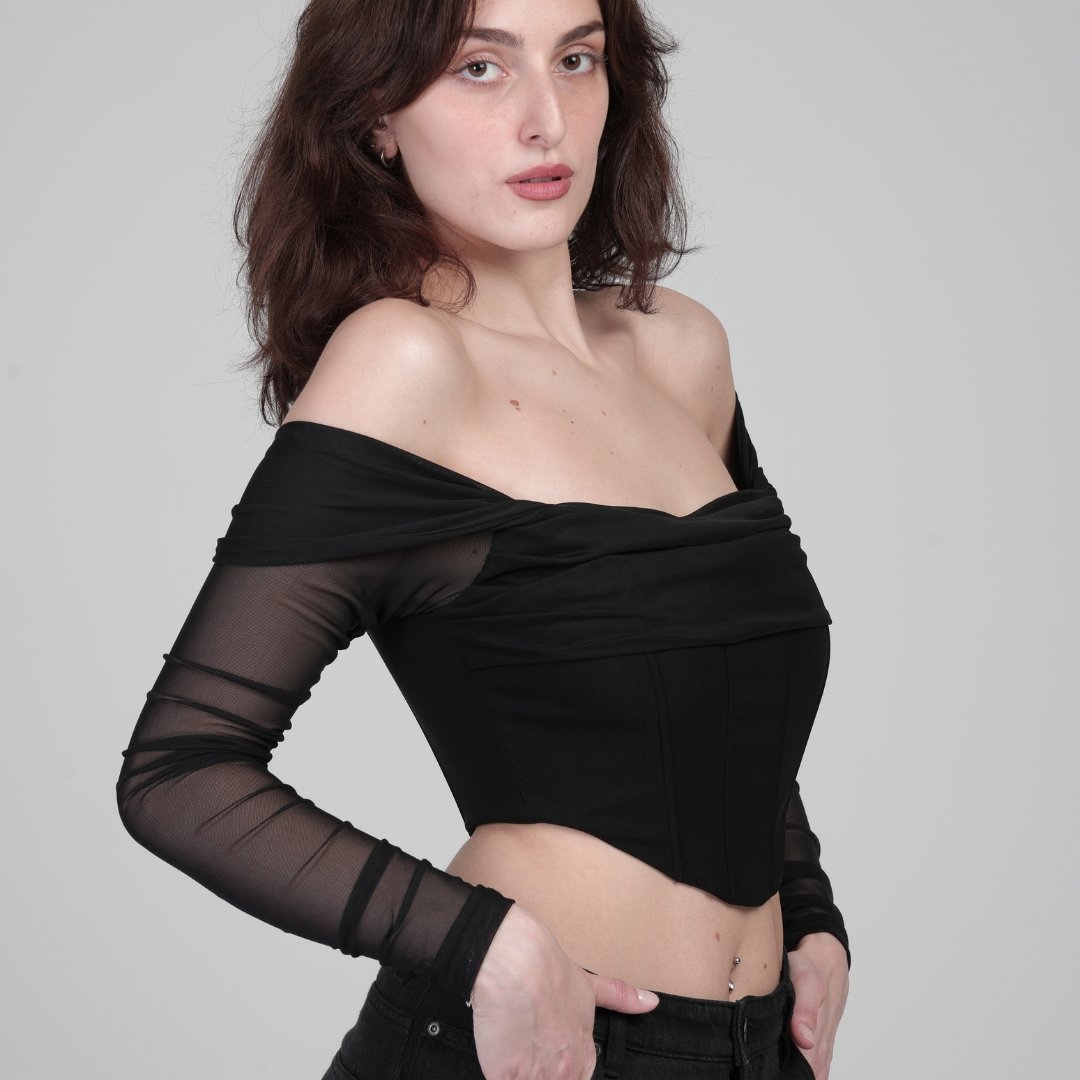 model in front of white background, stands to show side of black corset top with sleeves 
