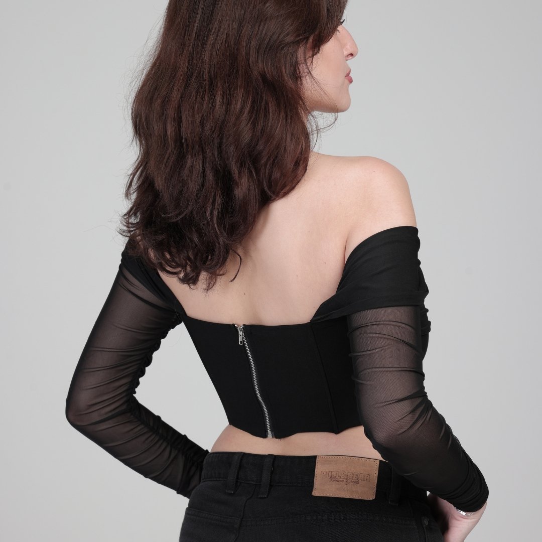 model in black corset top with sleeves sands with the back to show product 